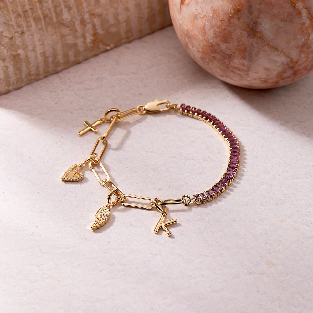  Priya Birthstone Charm Bracelet with a purple baguette tennis half and a chain half, dangling a cross, pavé heart, wing, and an initial letter charm.