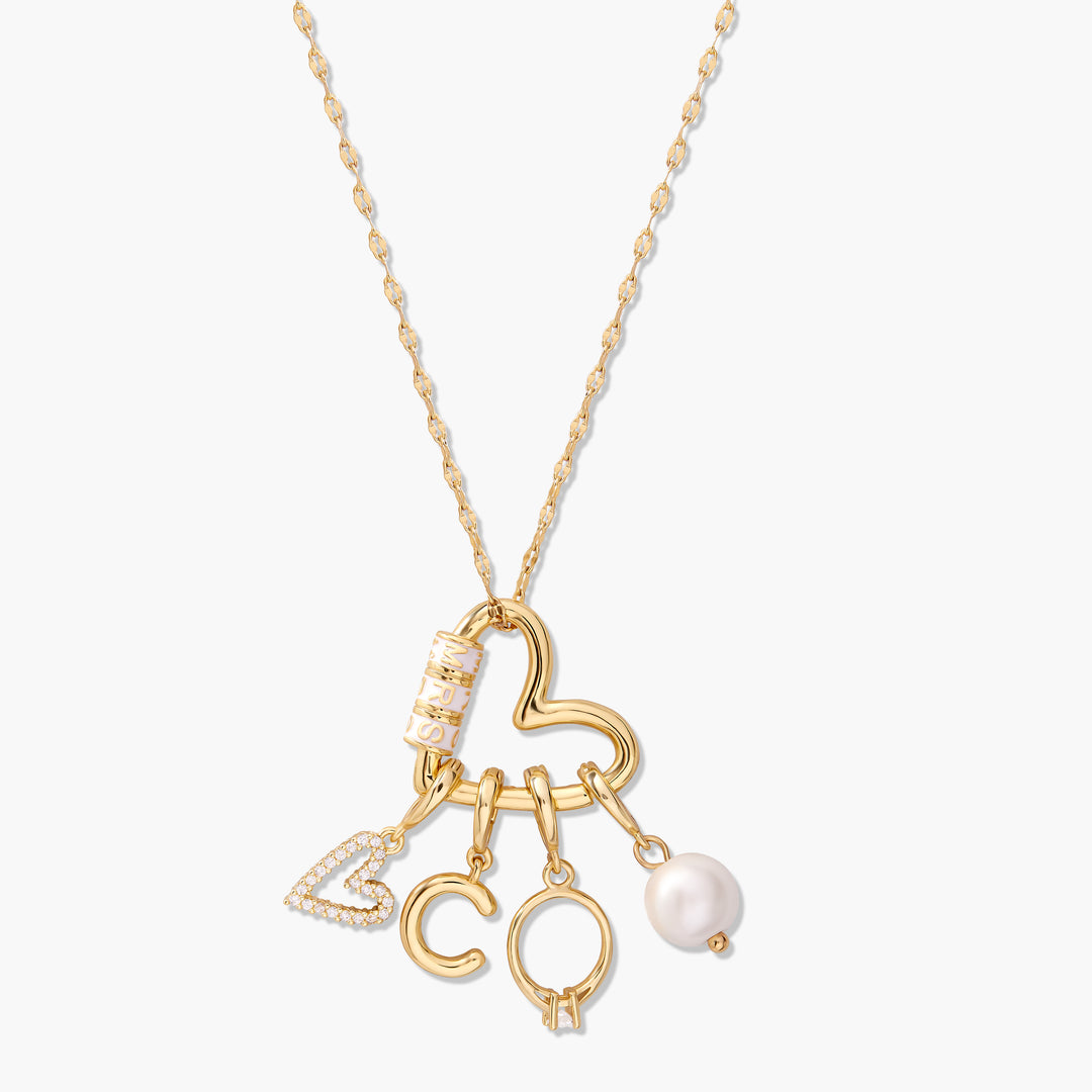 Gold-tone Mrs. Carabiner Charm Necklace with a heart-shaped ring clasp holding a pavé heart initial charm, a letter charm, a birthstone charm holder, an enamel name bead, and a pearl drop.
