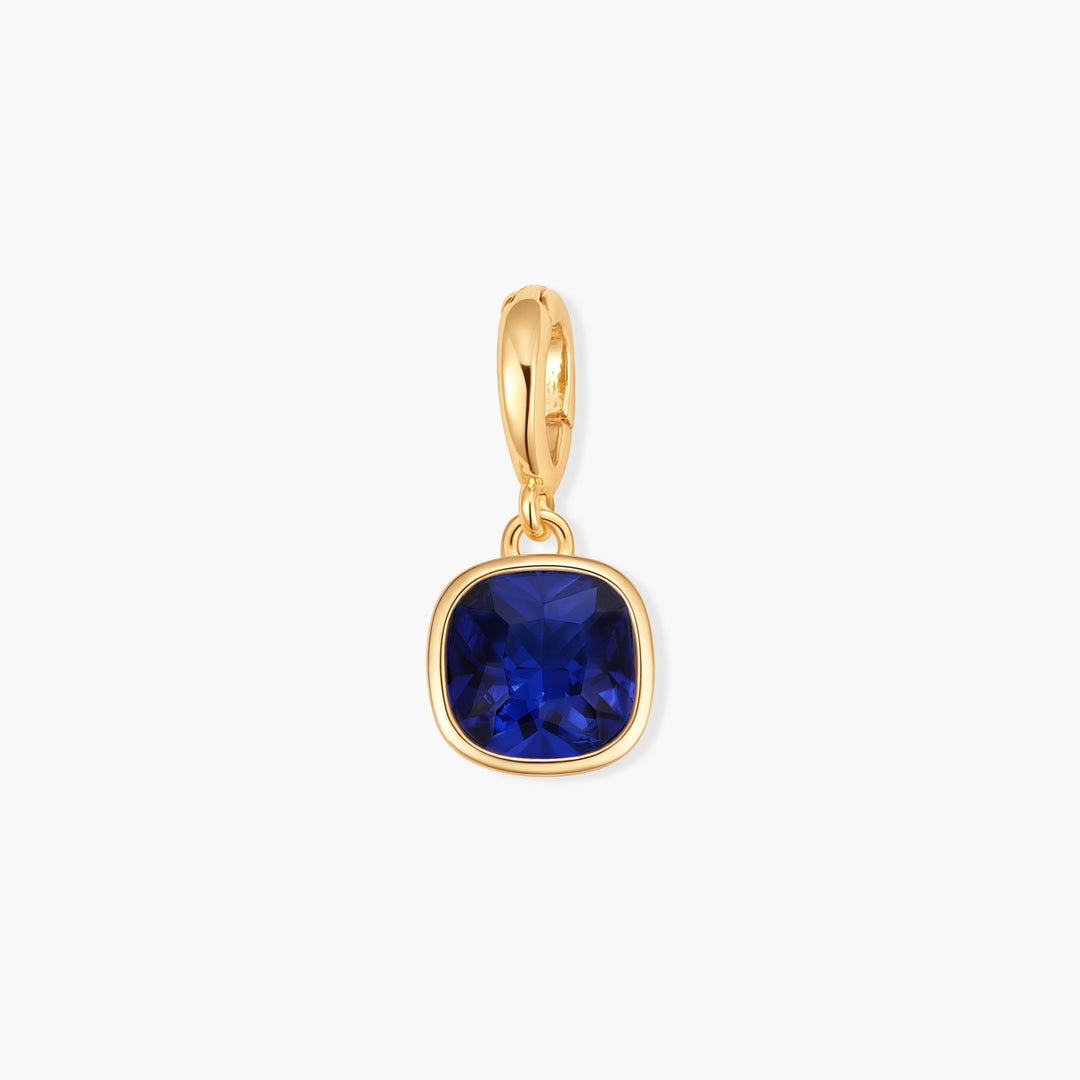 Gold-tone birthstone charm with a cushion-cut blue stone in a polished square bezel setting and ring clasp.