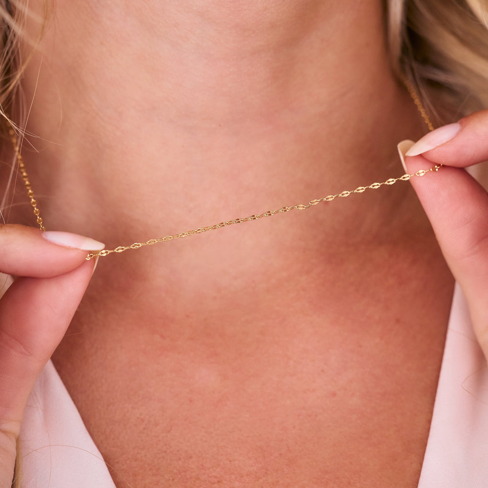  Celine Necklace, a delicate flat-link chain necklace with a twisted mirror finish, worn by a model at choker length.