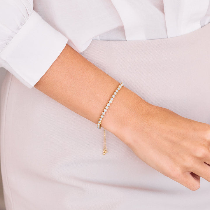  Bezel-set opal tennis bolo bracelet with an adjustable slide closure and dangling chain, worn by a model.