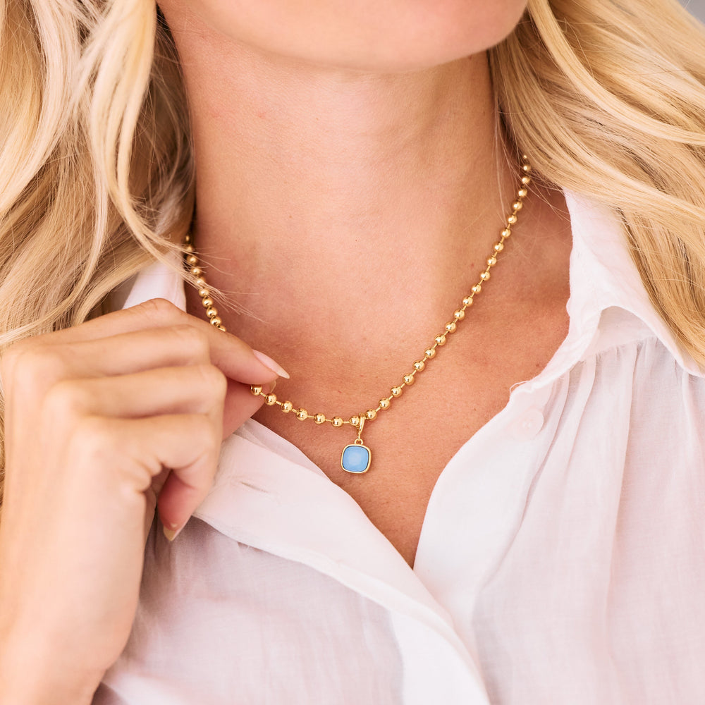 Pendant necklace with a cushion-cut blue opal bezel charm on a beaded chain, worn by a model.