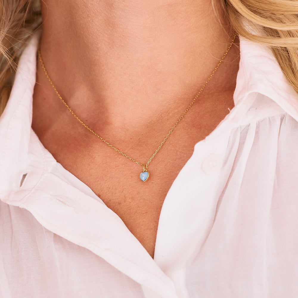  Heart pendant necklace with a bezel-set blue opal stone worn by a model, delicate chain catching light at the neckline.