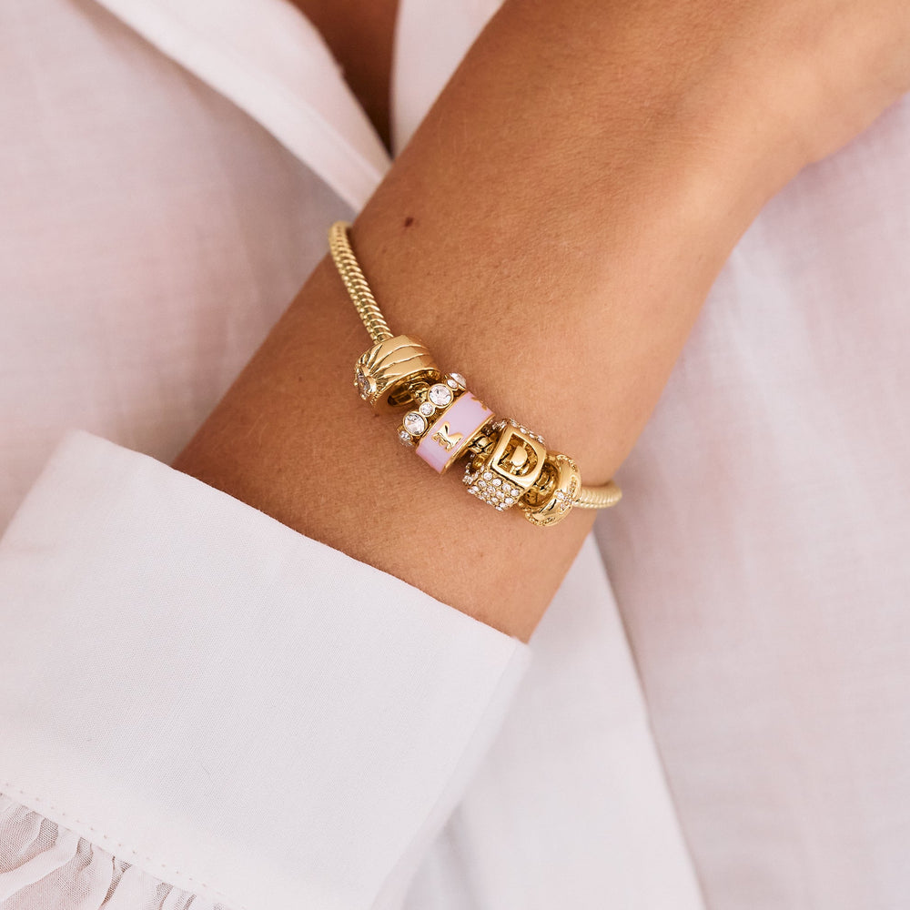 Charm bracelet with pink enamel initial beads, a crystal-pavé bead, and a ribbed heart charm, worn by a model.